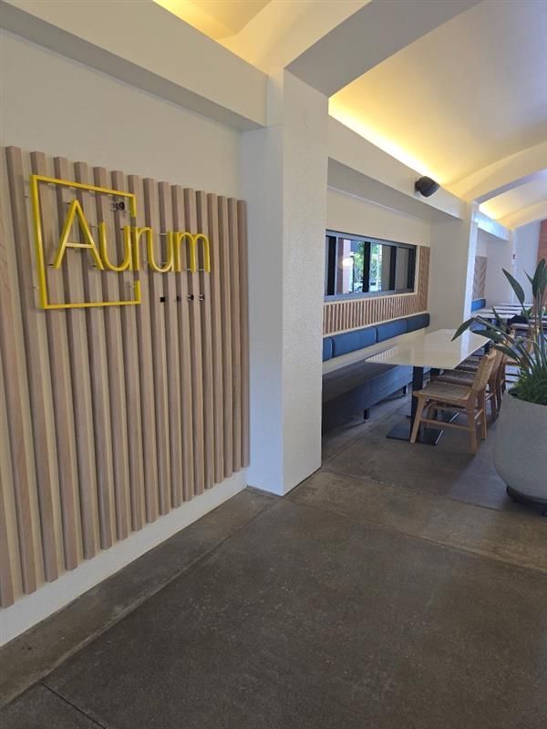 Entrance to Aurum restaurant: Gold logo, wooden wall, tables, benches.