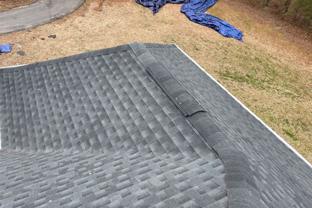 A roof is being installed on a house with a blue tarp on the ground.