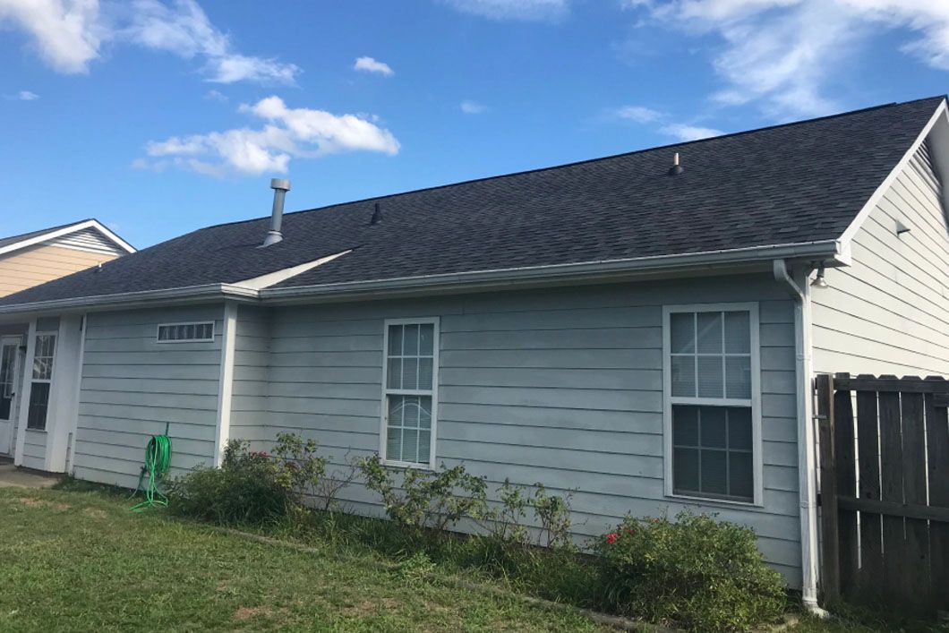 A white house with a black roof and a fence in front of it.