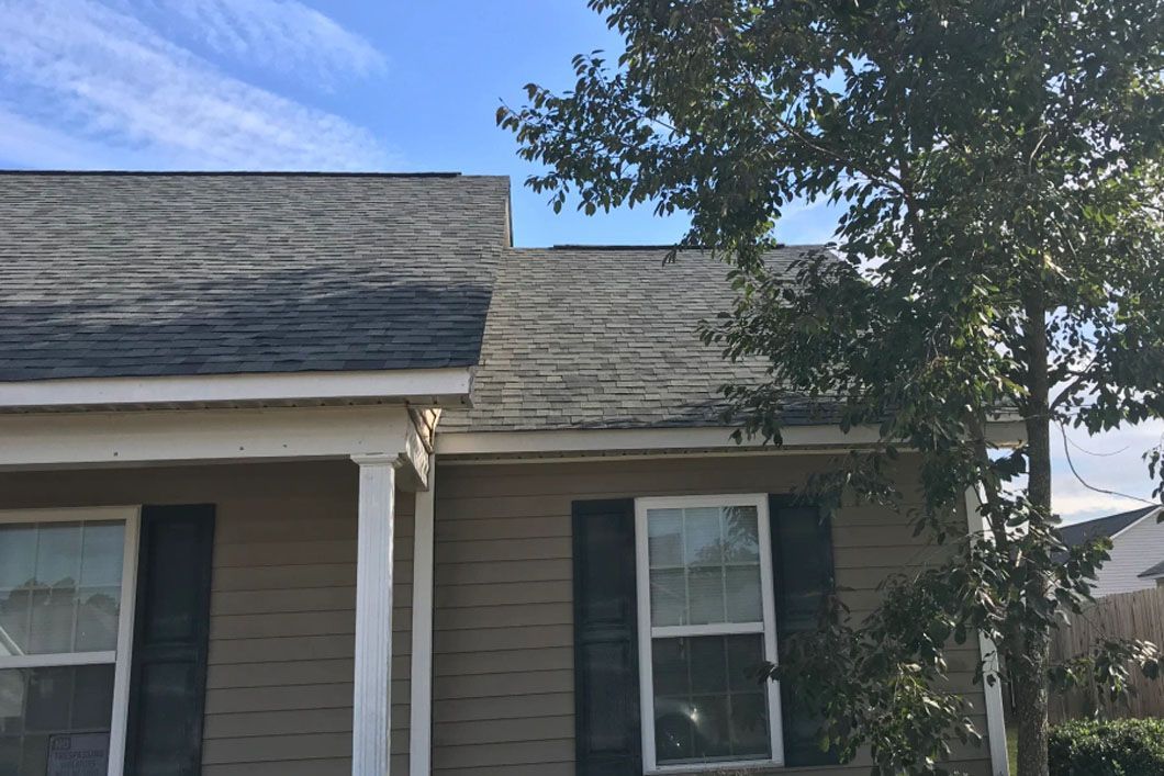 A house with a roof that is covered in shingles and a tree in front of it.