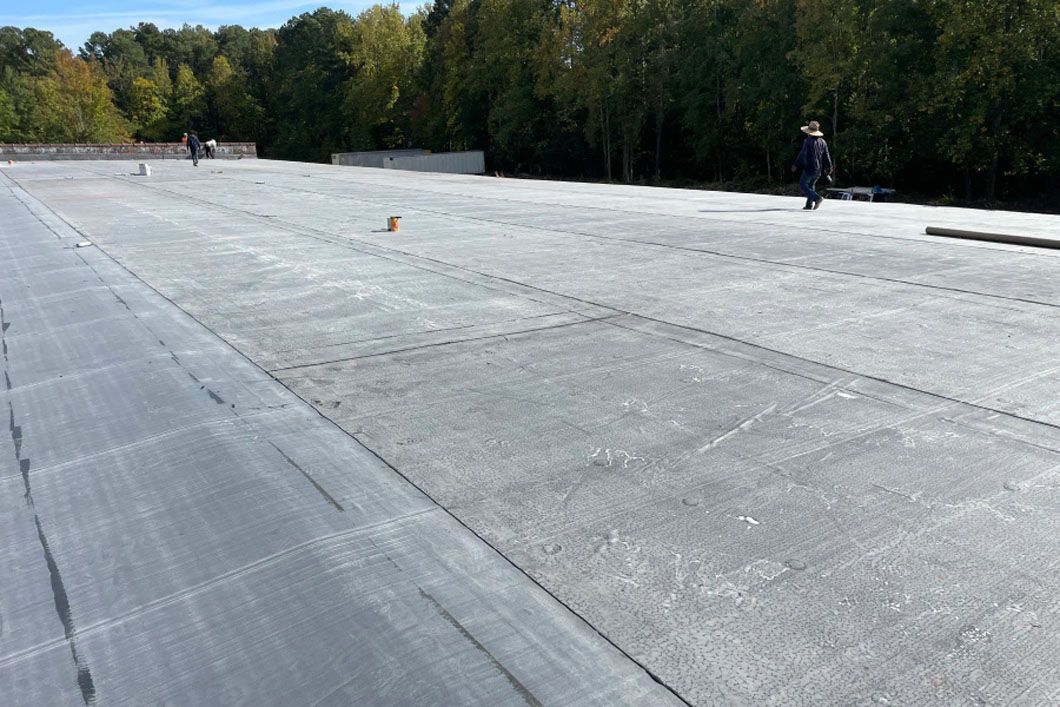 A man is standing on top of a roof with trees in the background.