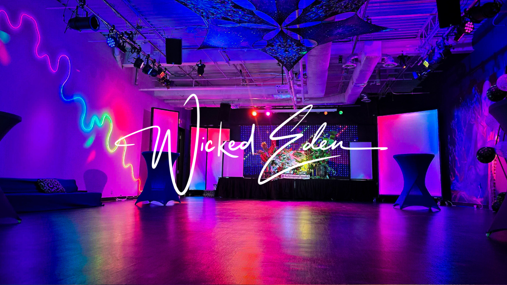 A large room with dark glossy floors is lit with rainbow light, glowing from panels and decorations