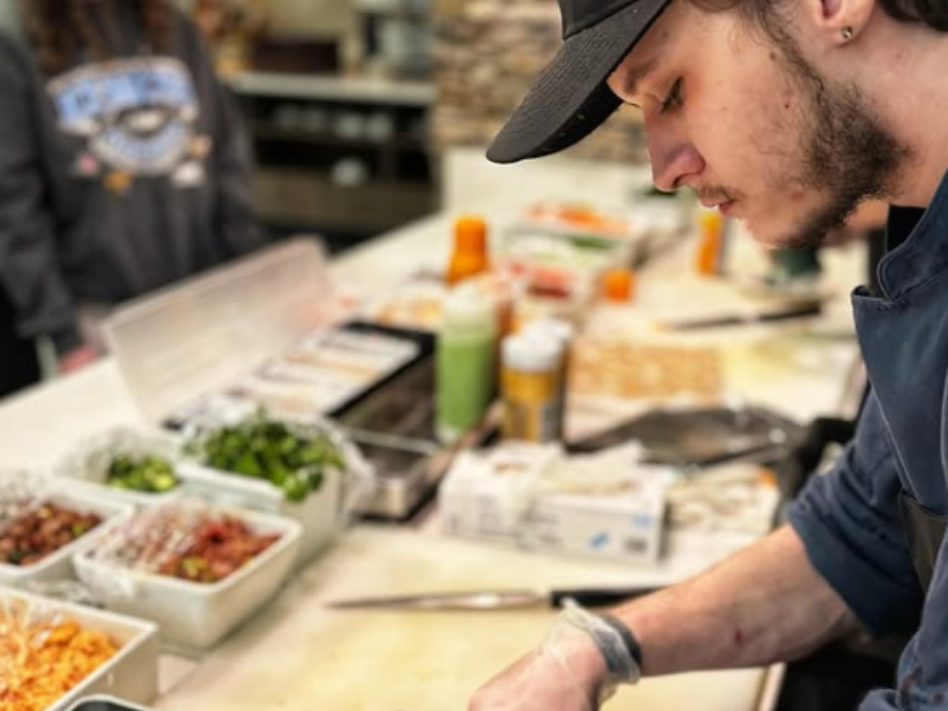 Chef wearing a hat preparing food on a counter with various ingredients in white containers.