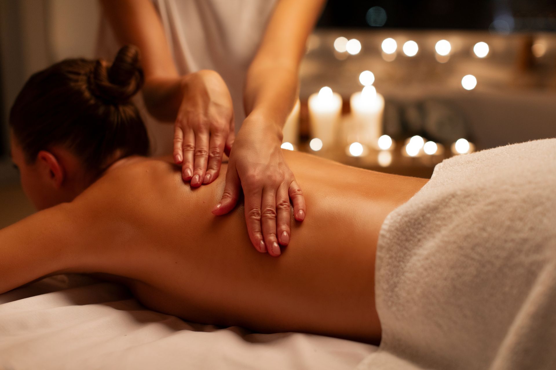 Hands massaging a person’s back in a candlelit spa setting