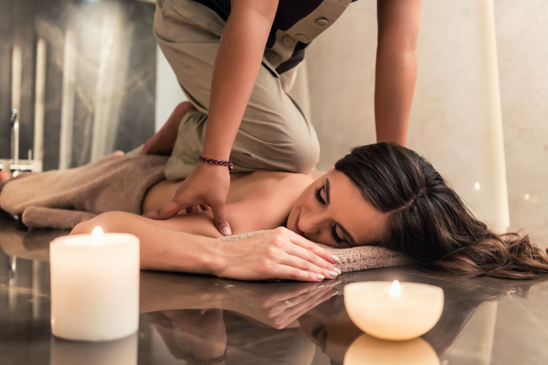 Person receiving a shoulder massage beside lit candles on a polished floor