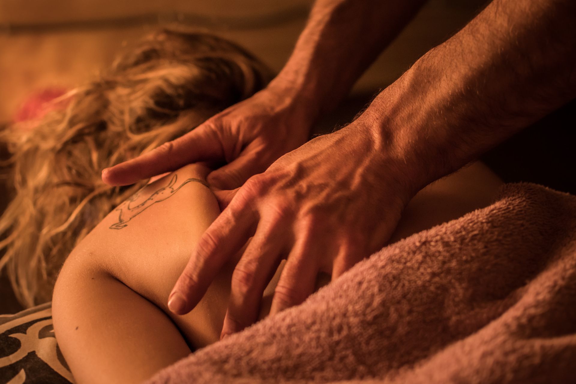 Hands giving a back massage with a towel in warm, dim lighting