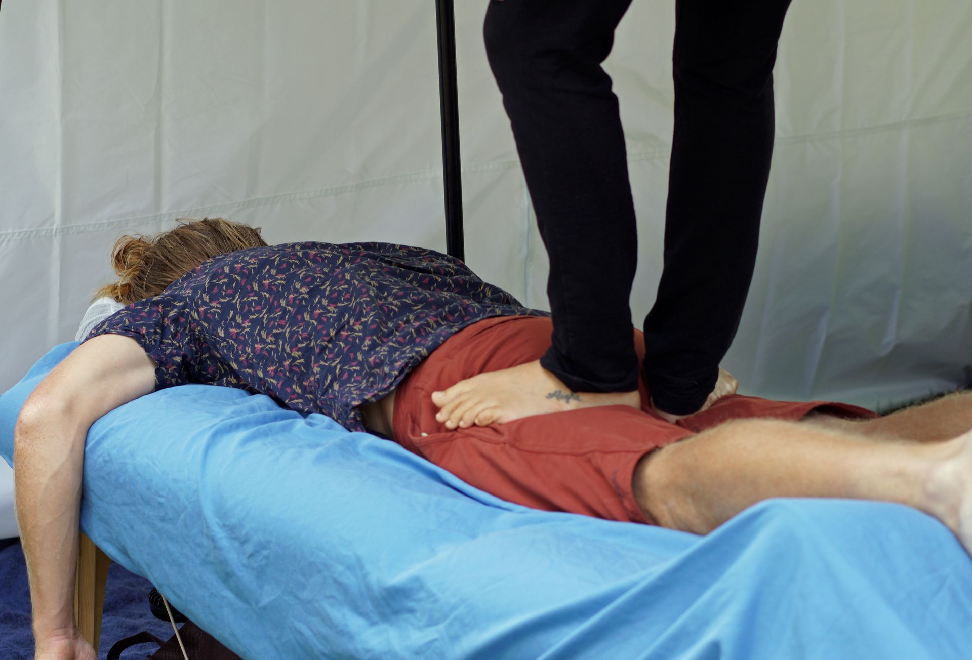 Person lying face down on a blue table while another person performs a back massage.