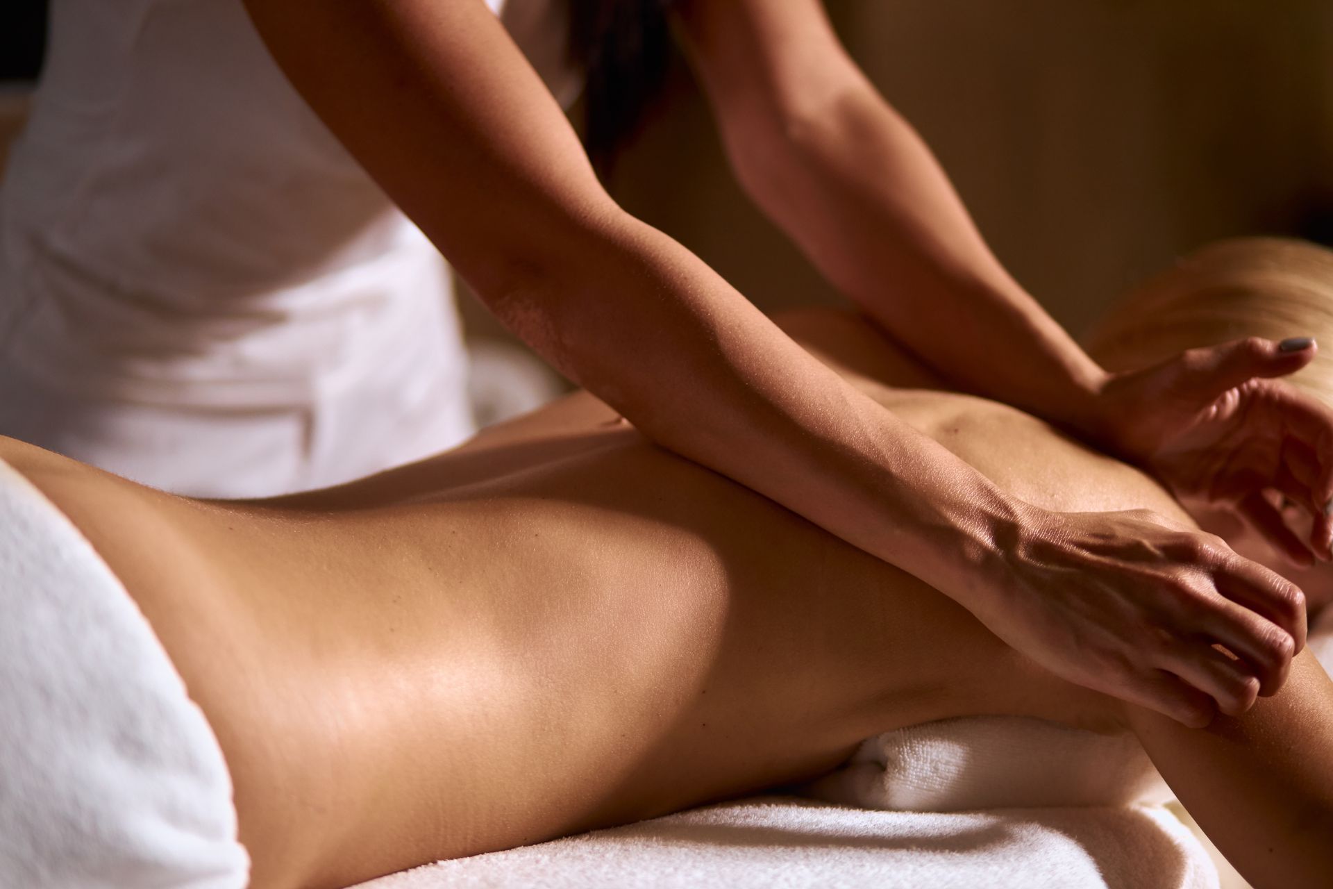 Hands massage a person’s back on a spa bed with white towels.