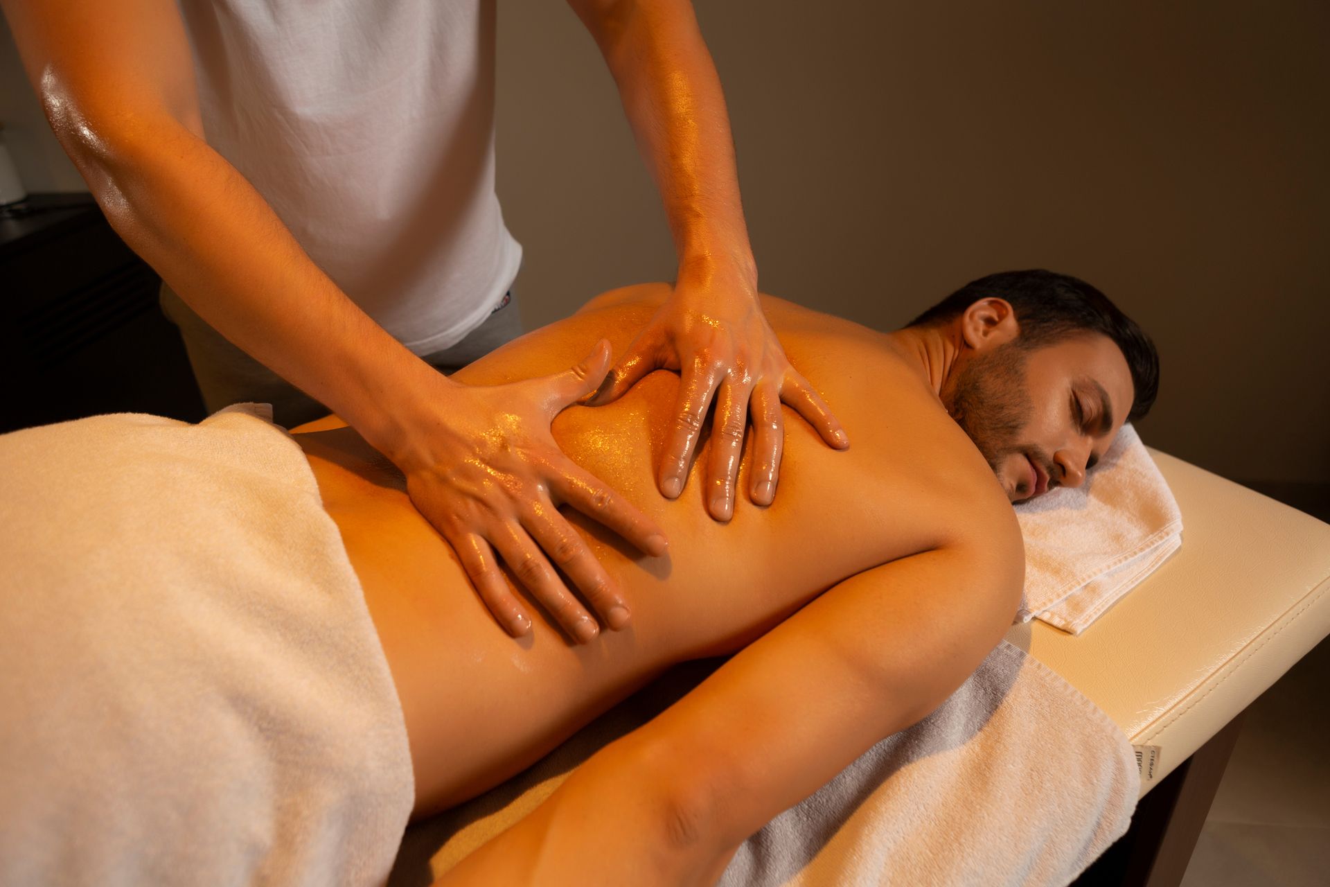 Massage therapist applying oil to a client lying face down on a massage table