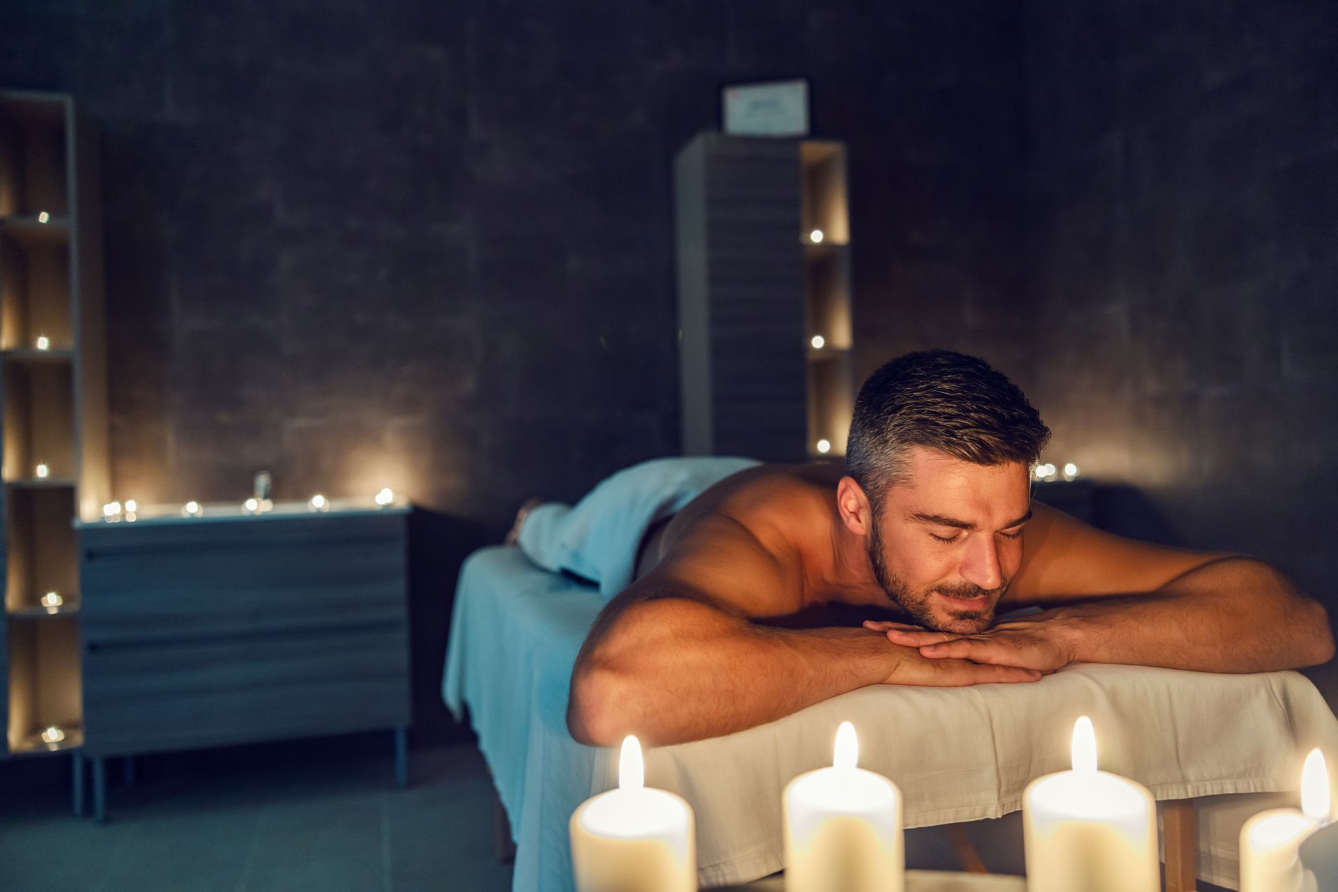 Man relaxing on a massage table with lit candles in a dim spa room