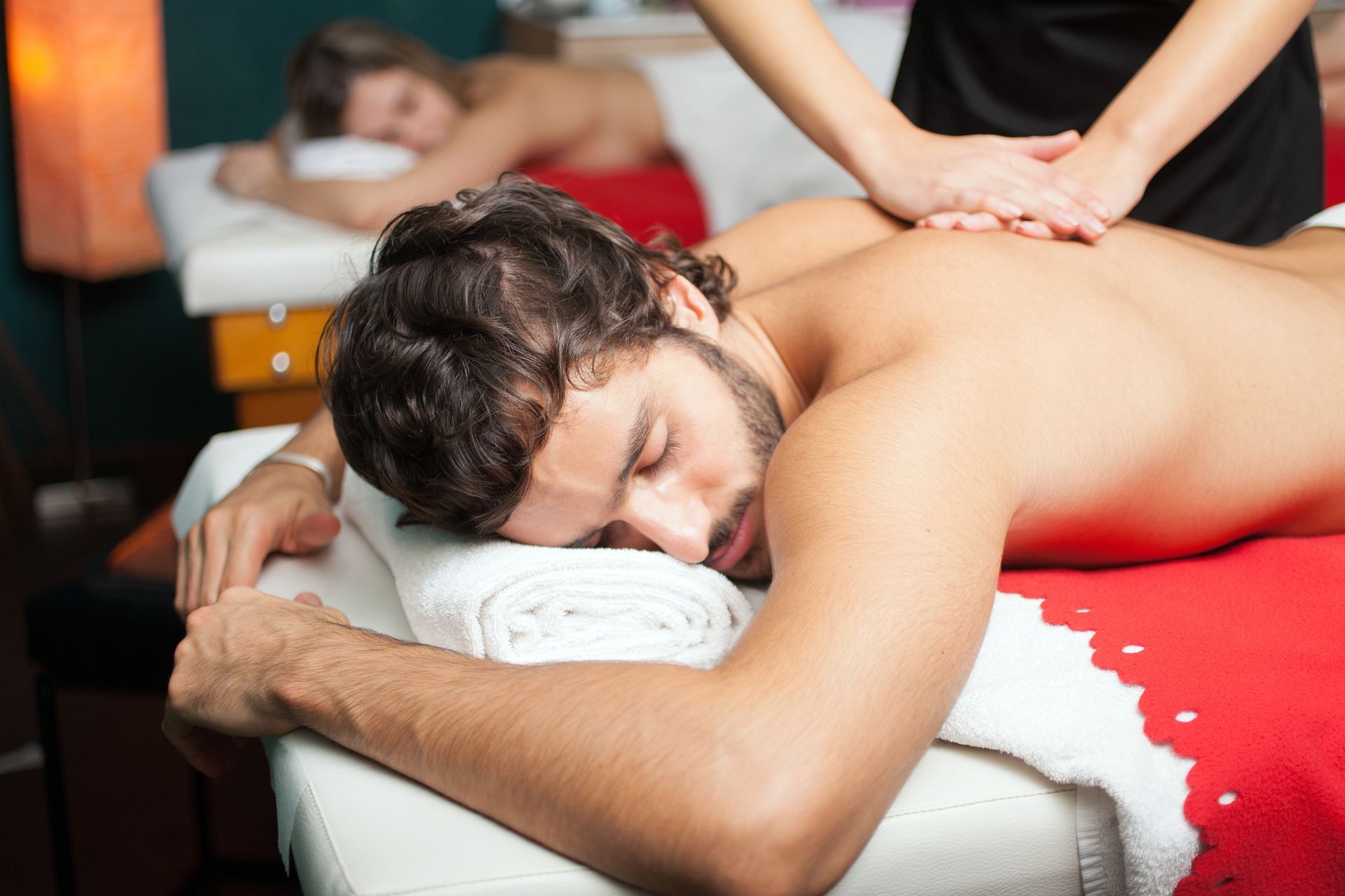Person receiving a back massage on a spa table, with another person working in the background