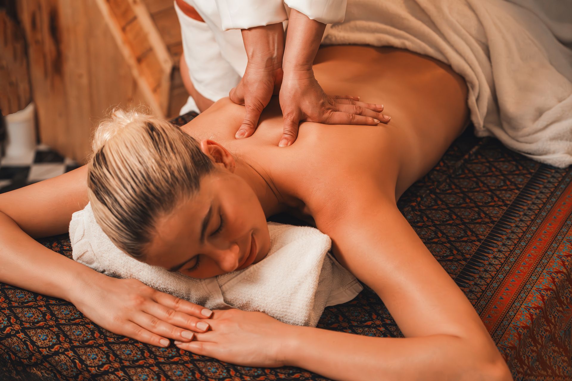 Massage therapist giving a back massage to a person lying face down on a mat with a towel