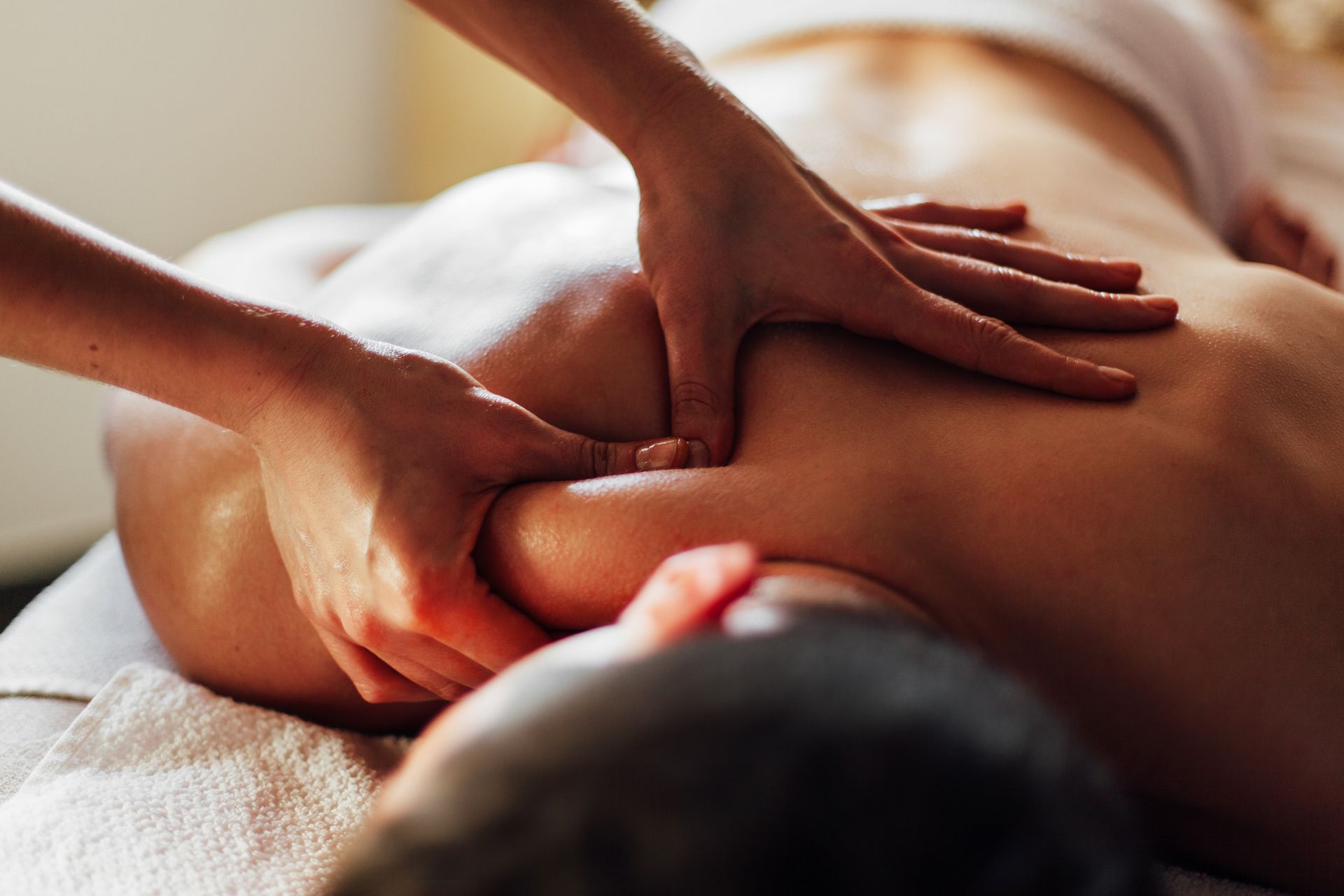 Hands giving a back massage on a person lying face down on a white bed