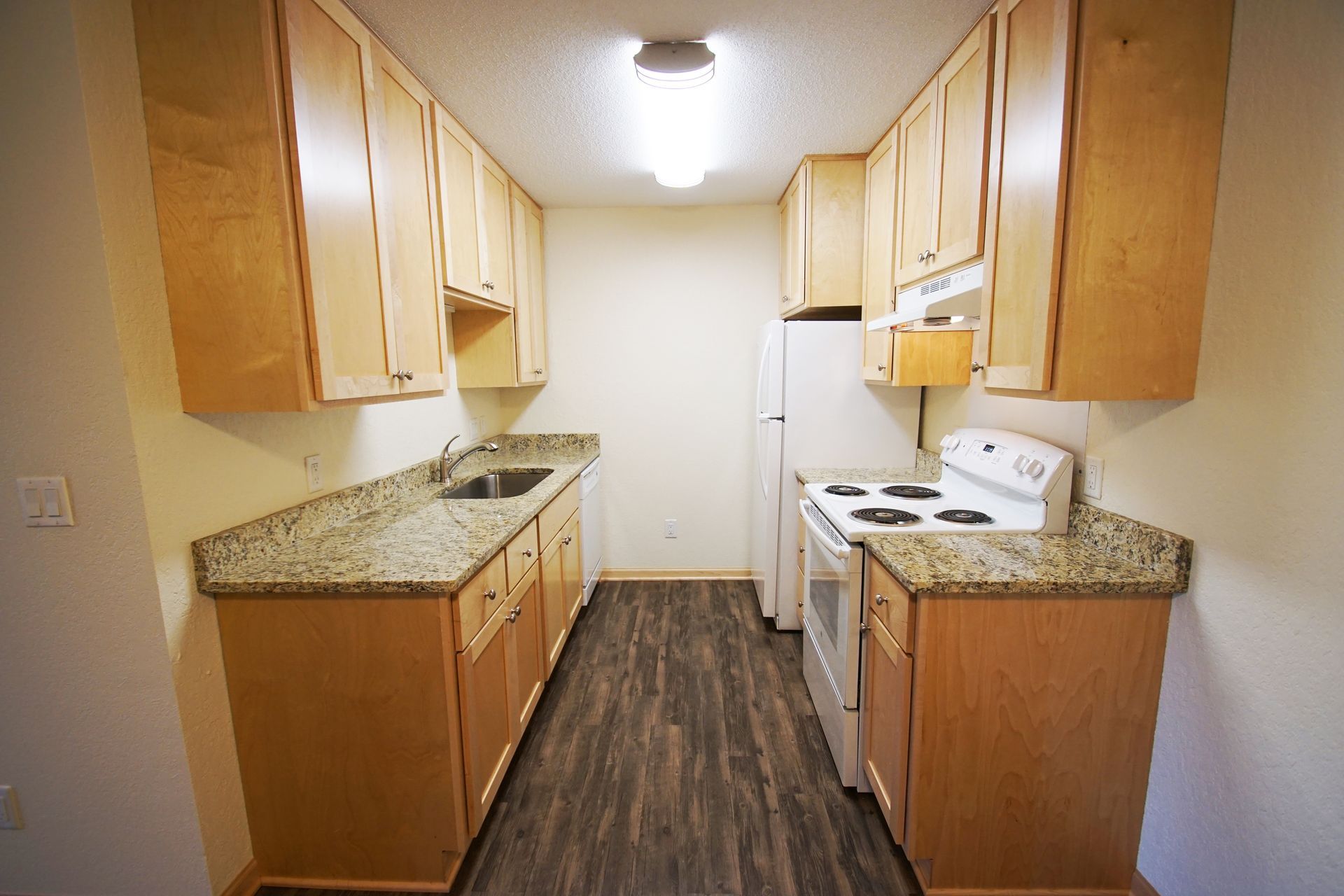 a kitchen with wooden cabinets , granite counter tops , a stove , refrigerator and sink .
