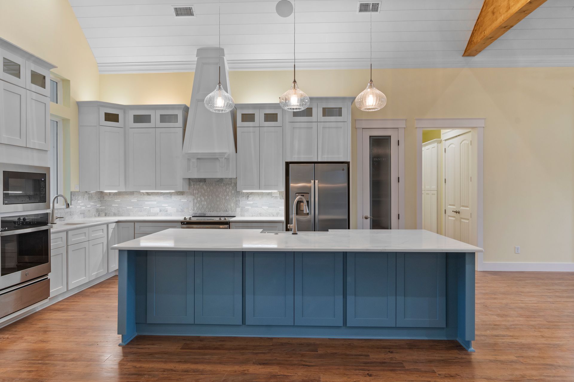 A kitchen with blue cabinets , white cabinets , stainless steel appliances and a large island.