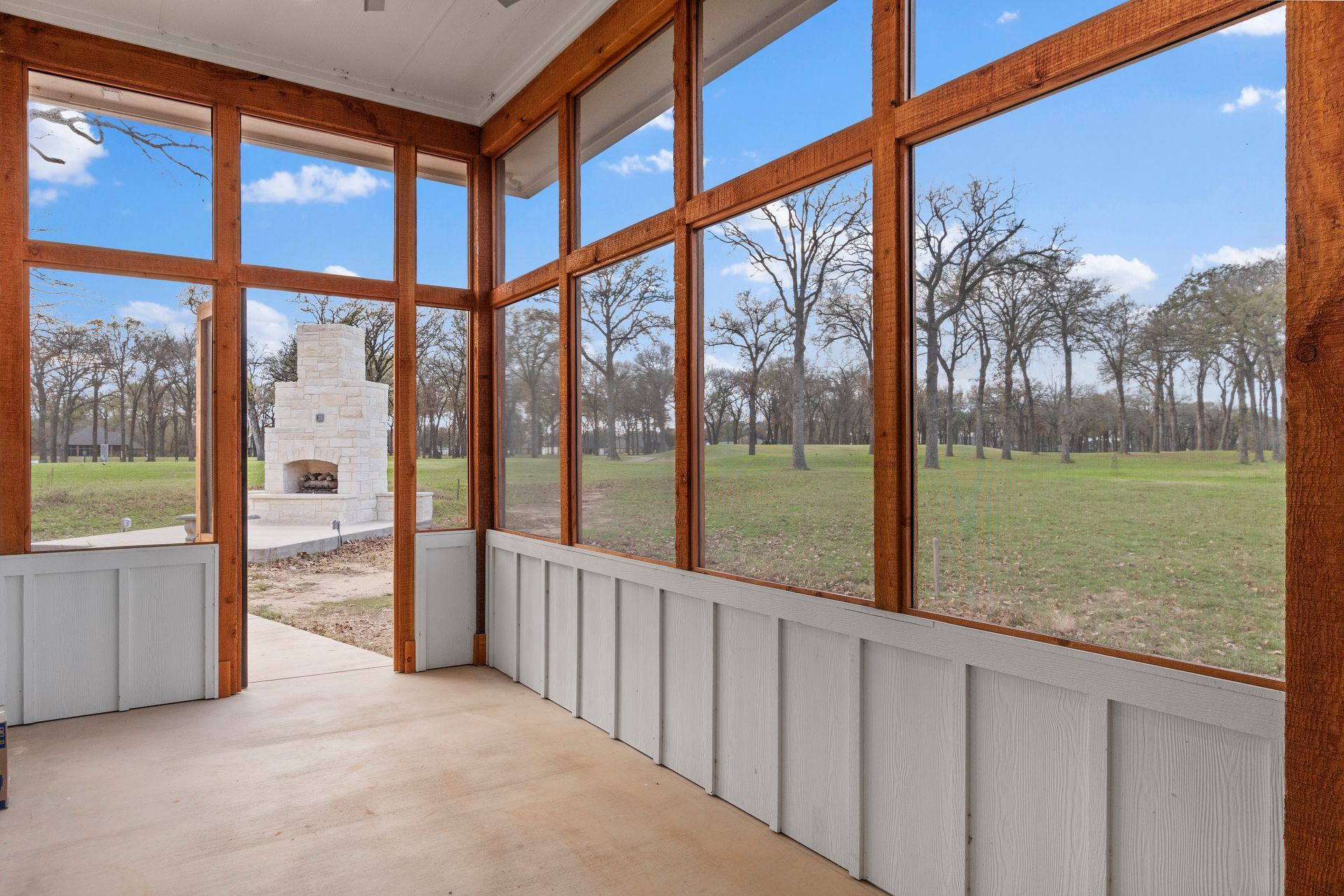 A screened in porch with a fireplace and trees in the background.