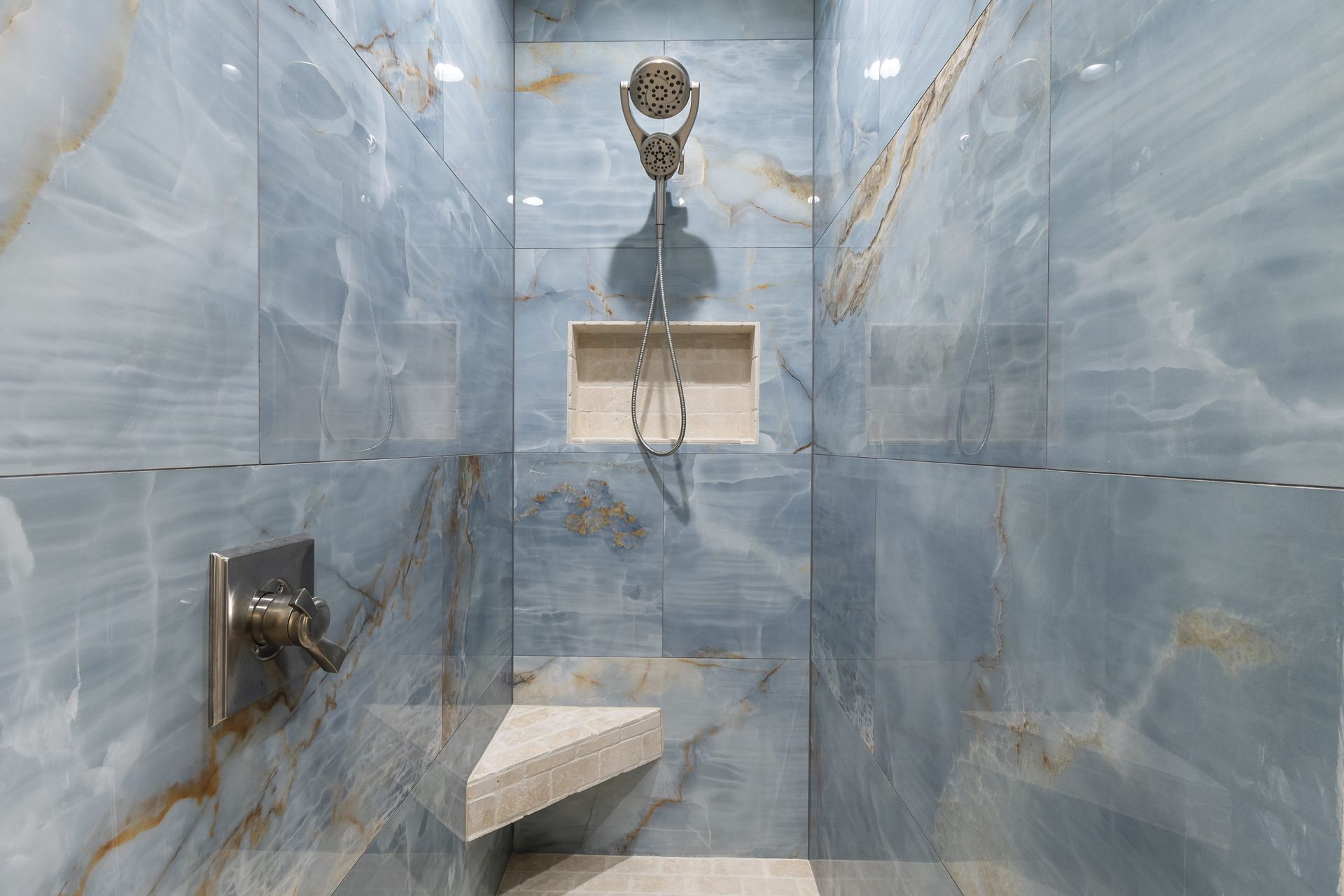 A bathroom with blue tiles and a walk in shower with a bench.