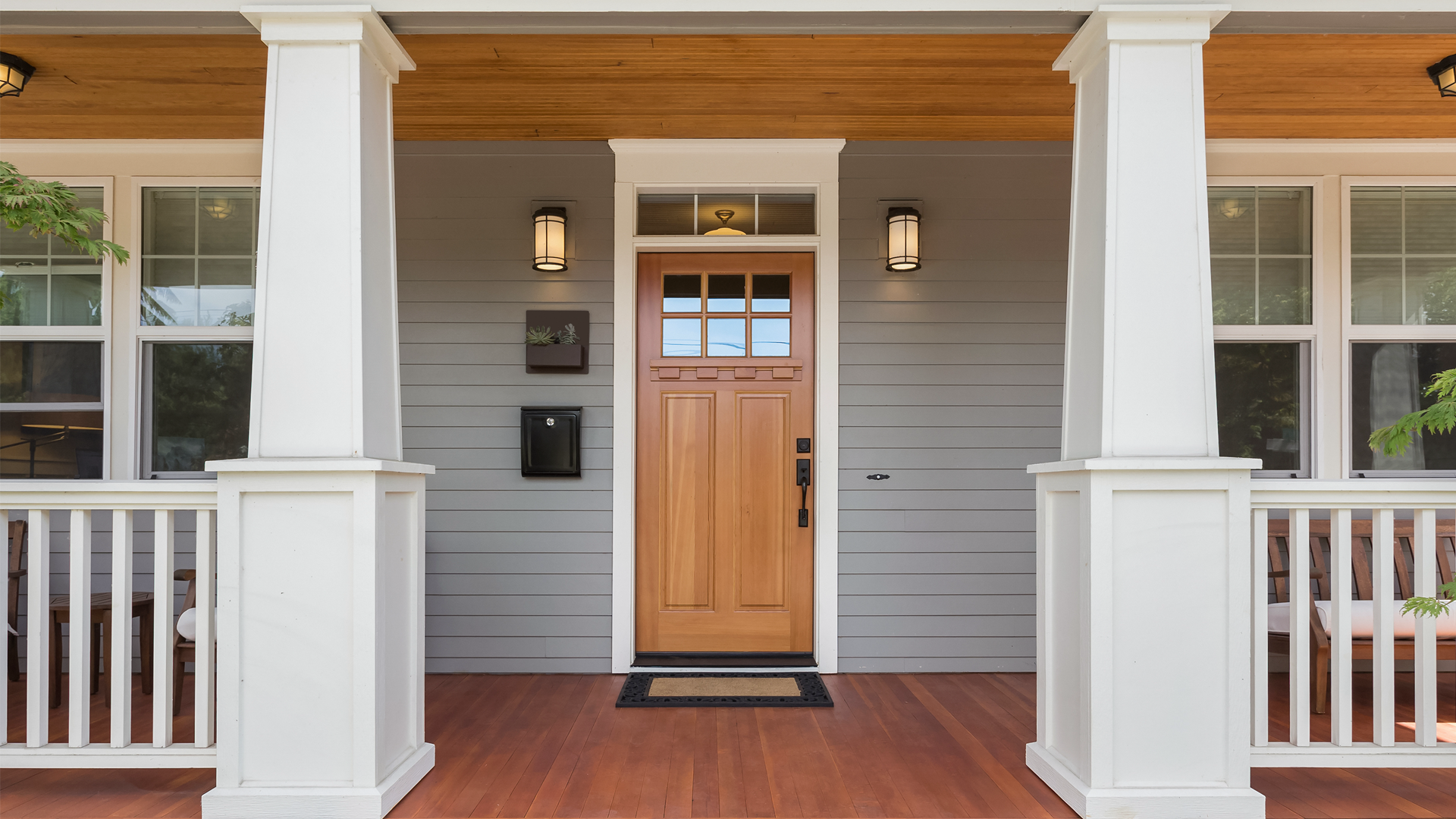 A front porch of a house with a wooden door and white pillars.