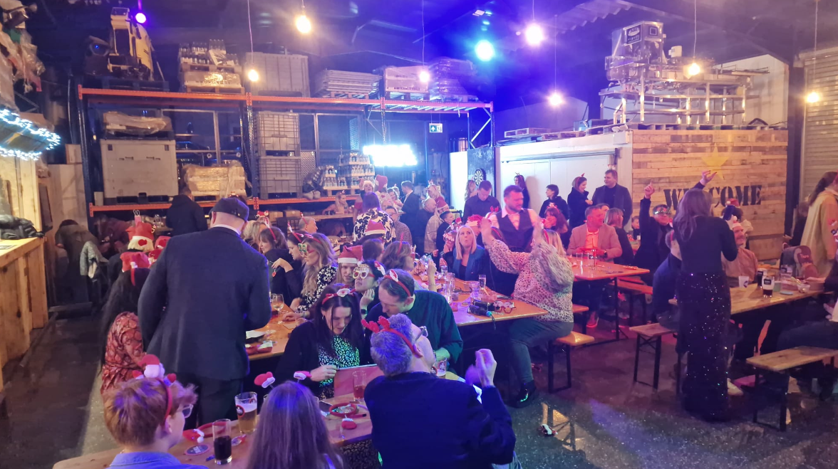 A large group of people are standing around tables in a warehouse.