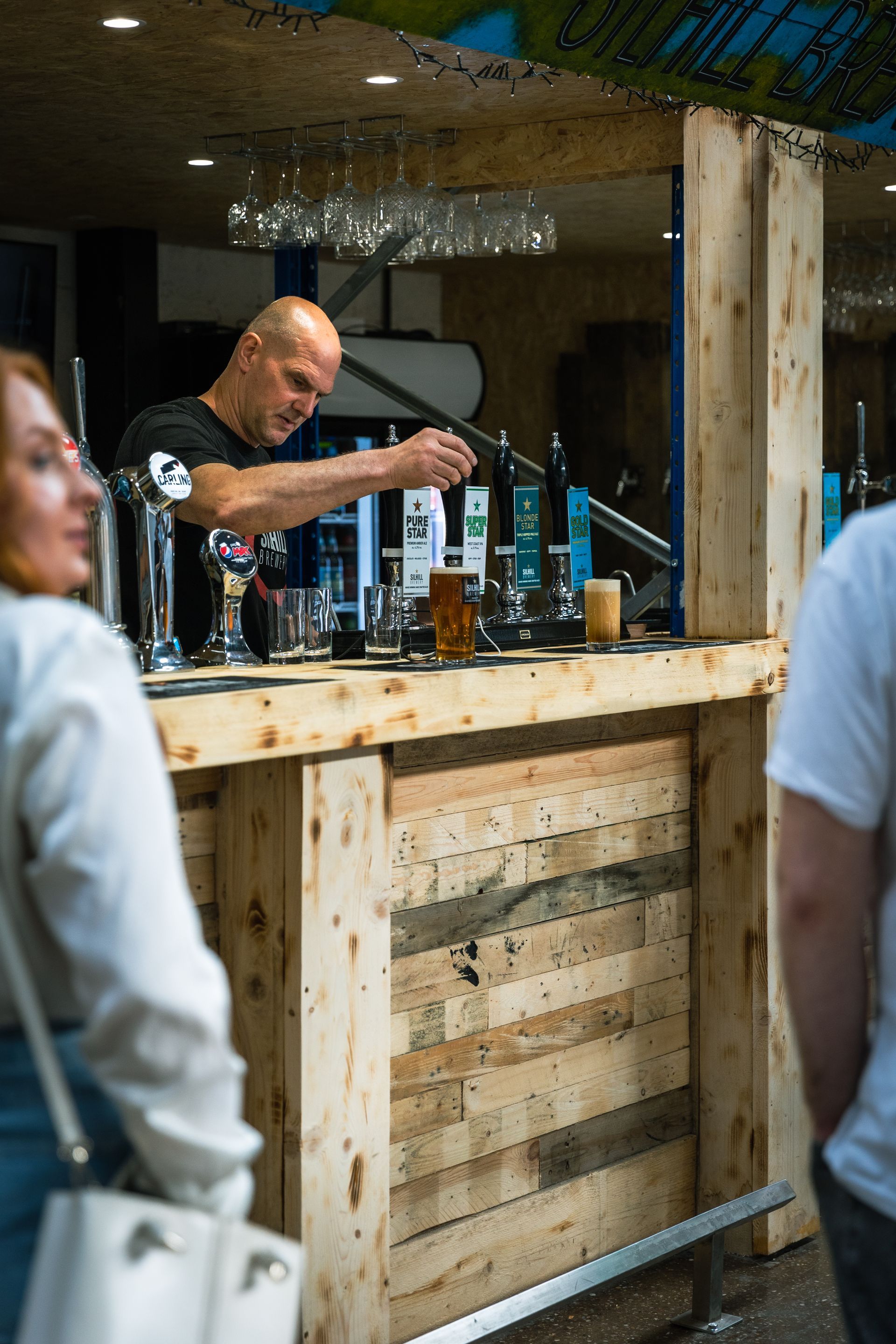 A man is pouring beer into a glass at a wooden bar.