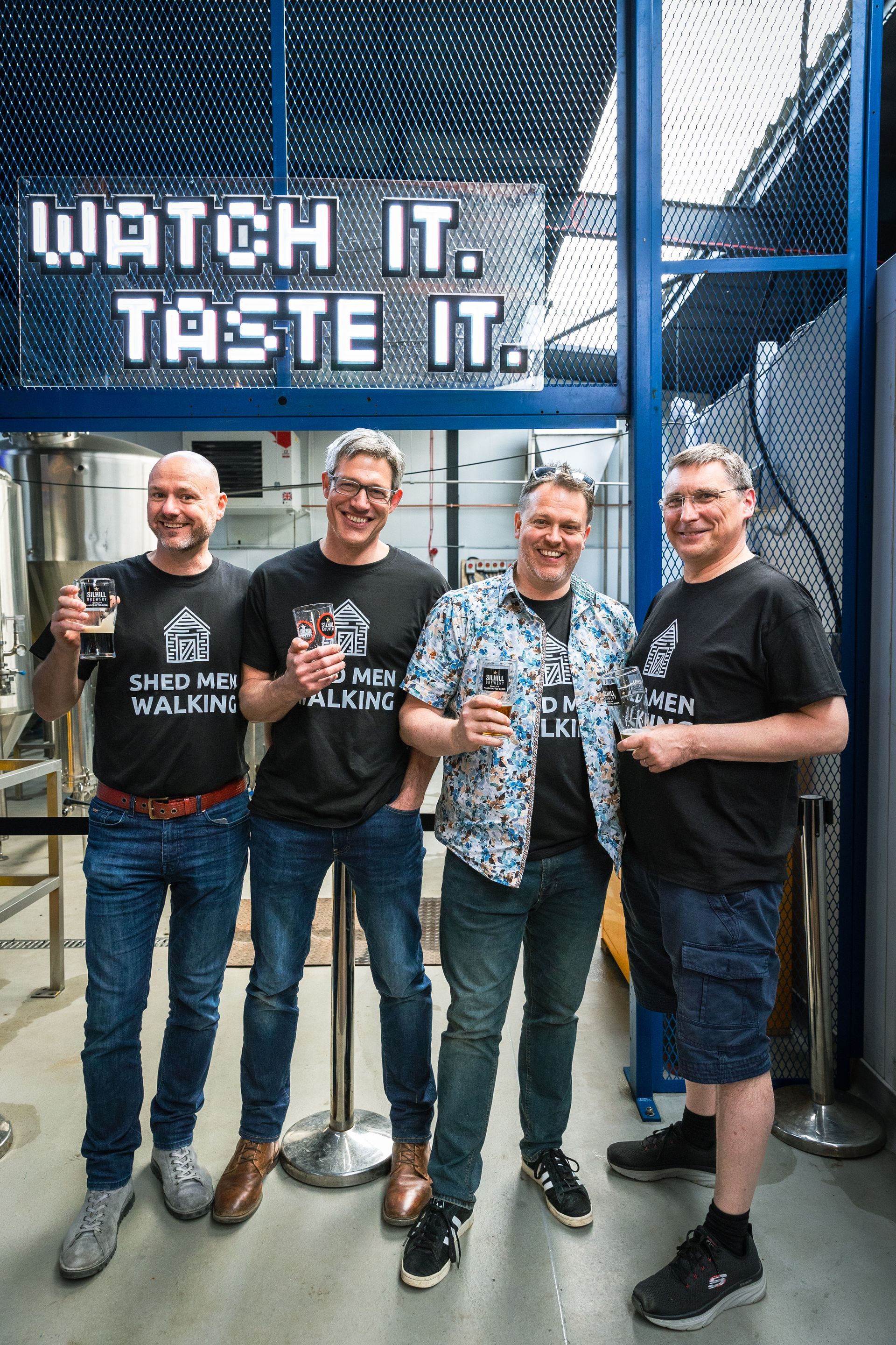 A group of men are standing next to each other in front of a sign that says watch it taste it.