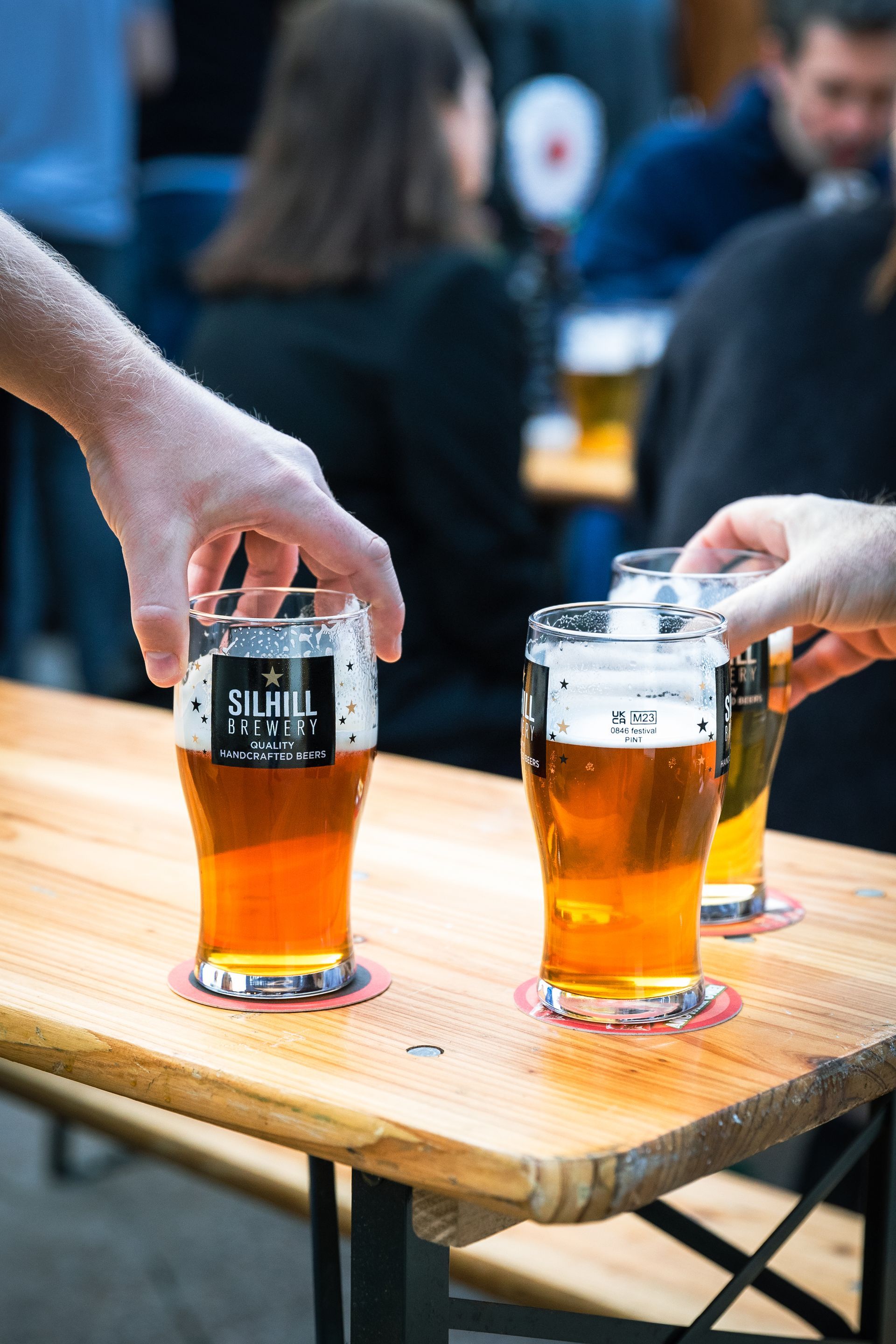 Three glasses of beer are sitting on a wooden table.