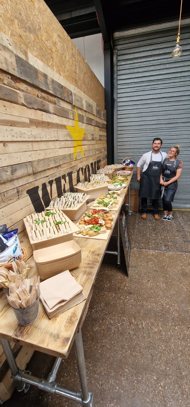 A couple of people standing next to a long table filled with food.