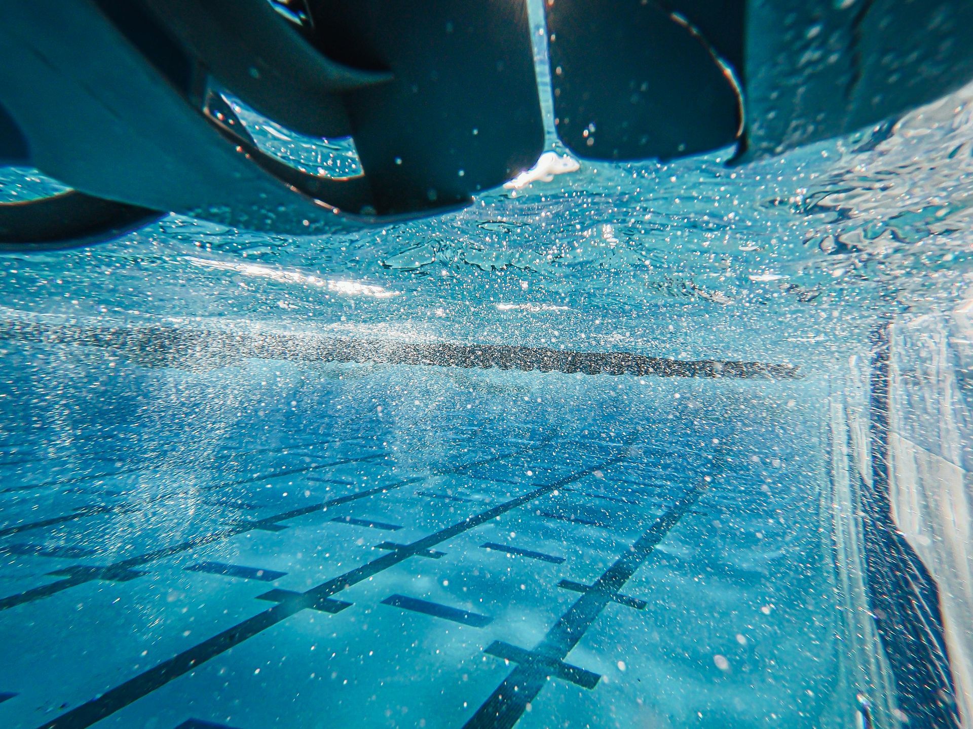 Underwater view of a swimming pool with lane markers, bubbles, and swim fins overhead.