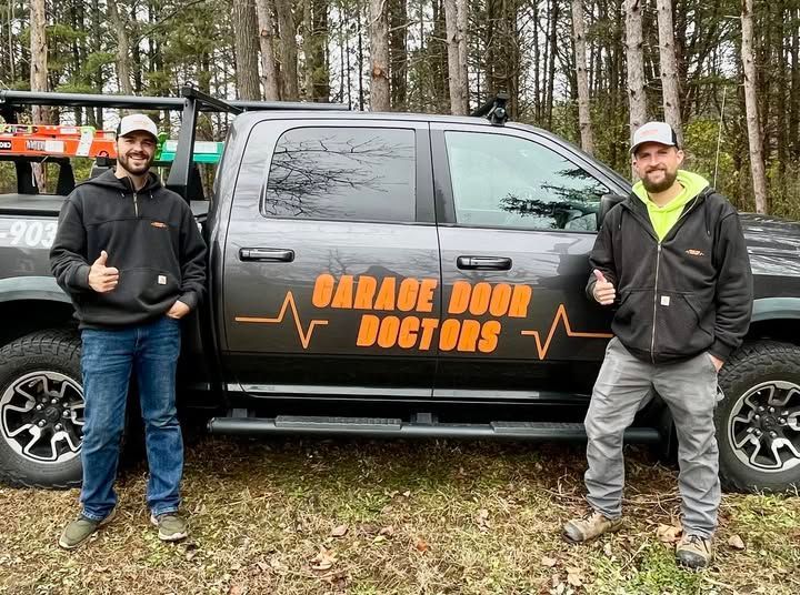 Two men are standing in front of a garage door doctors truck.