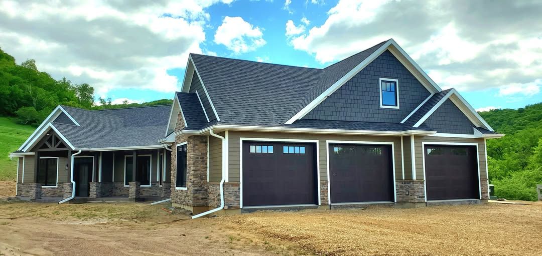 A large house with two garage doors is sitting on top of a dirt field.