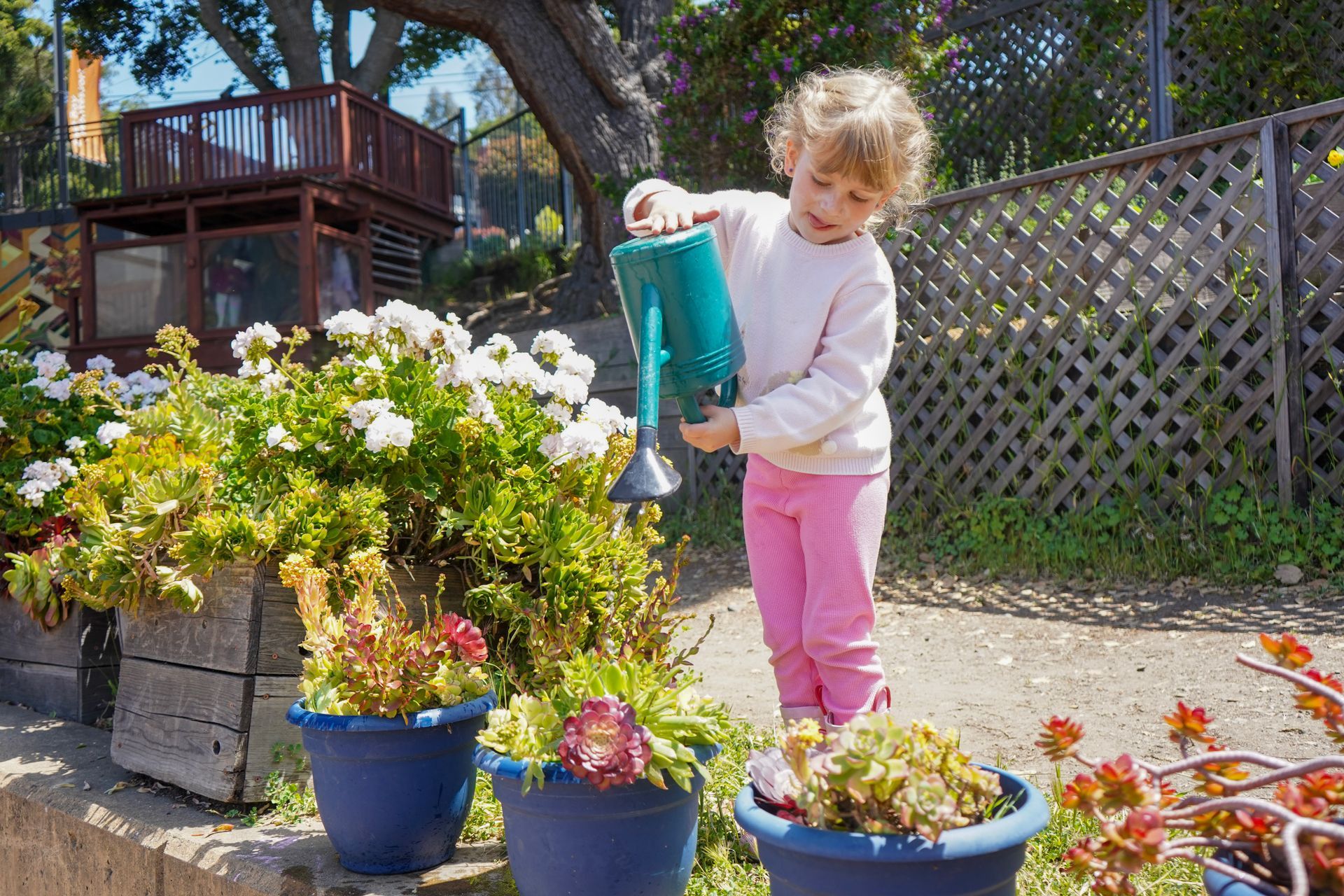 A young child waters the garden on the playground.
