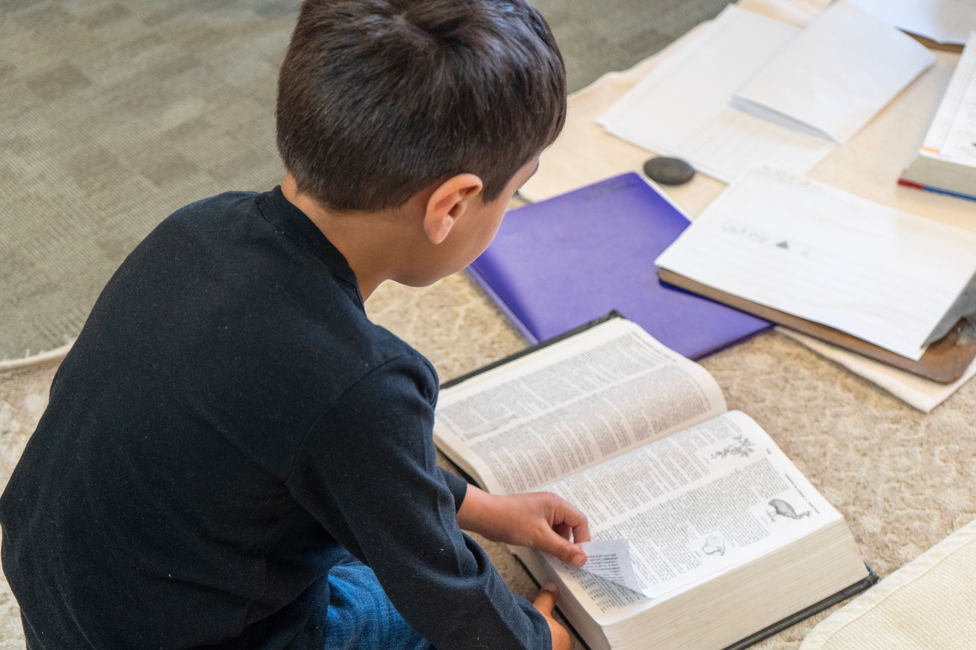 A Lower Elementary student looking up proper spelling with the Dictionary. The Montessori philosophy highlights self directed research.