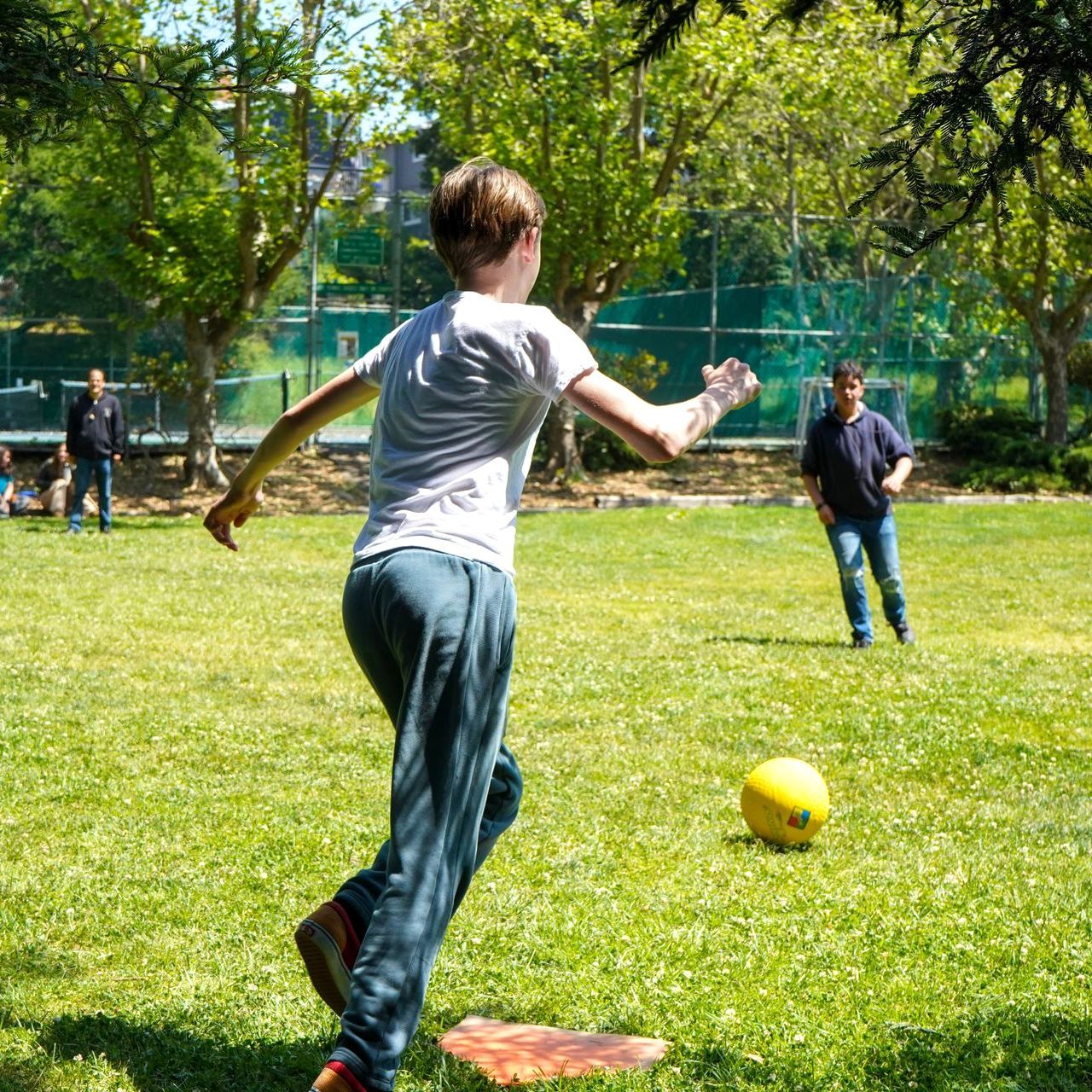 A middle school student plays kickball with his classmates in park during PE.