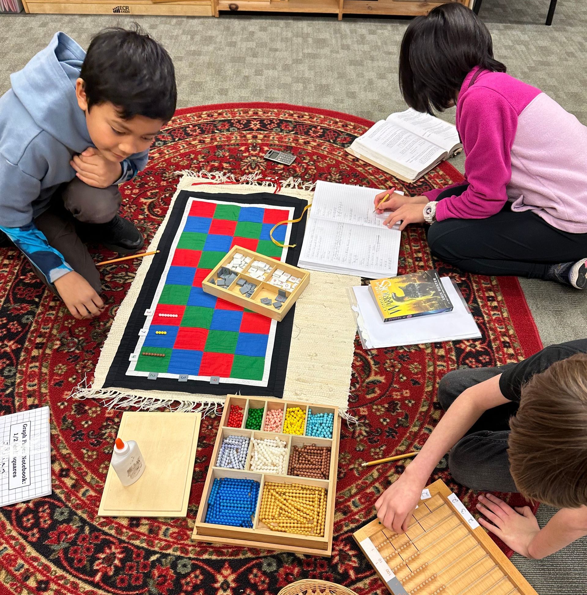 Three Upper Elementary students working together on a Montessori math material called the Checkerboard. Checkerboard is for long form multiplication.