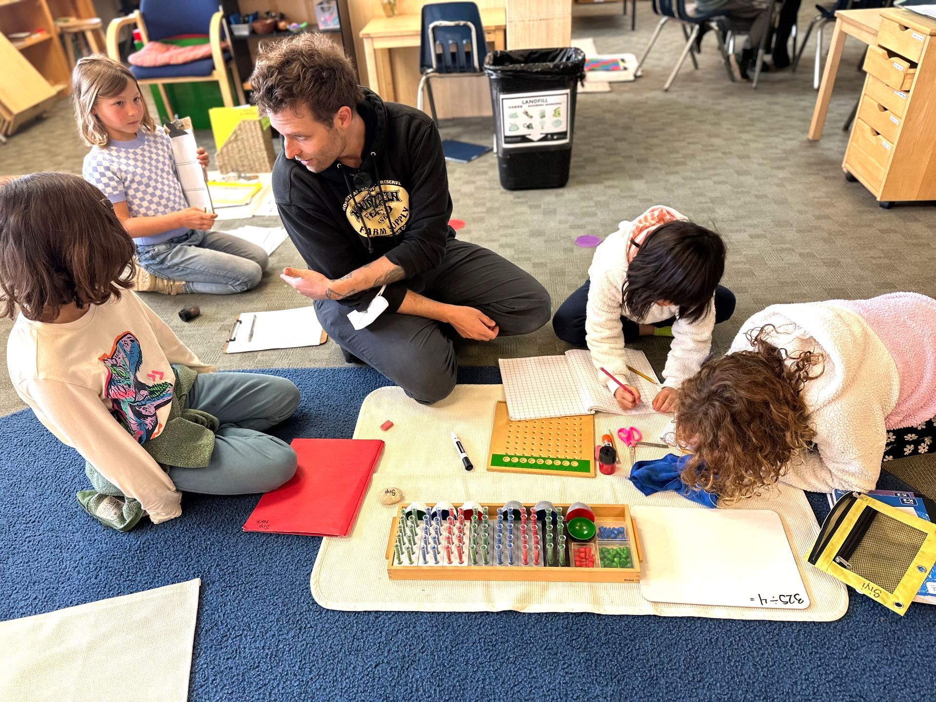 A Lower Elementary teacher presents a Montessori math lesson about long division to a group of students.