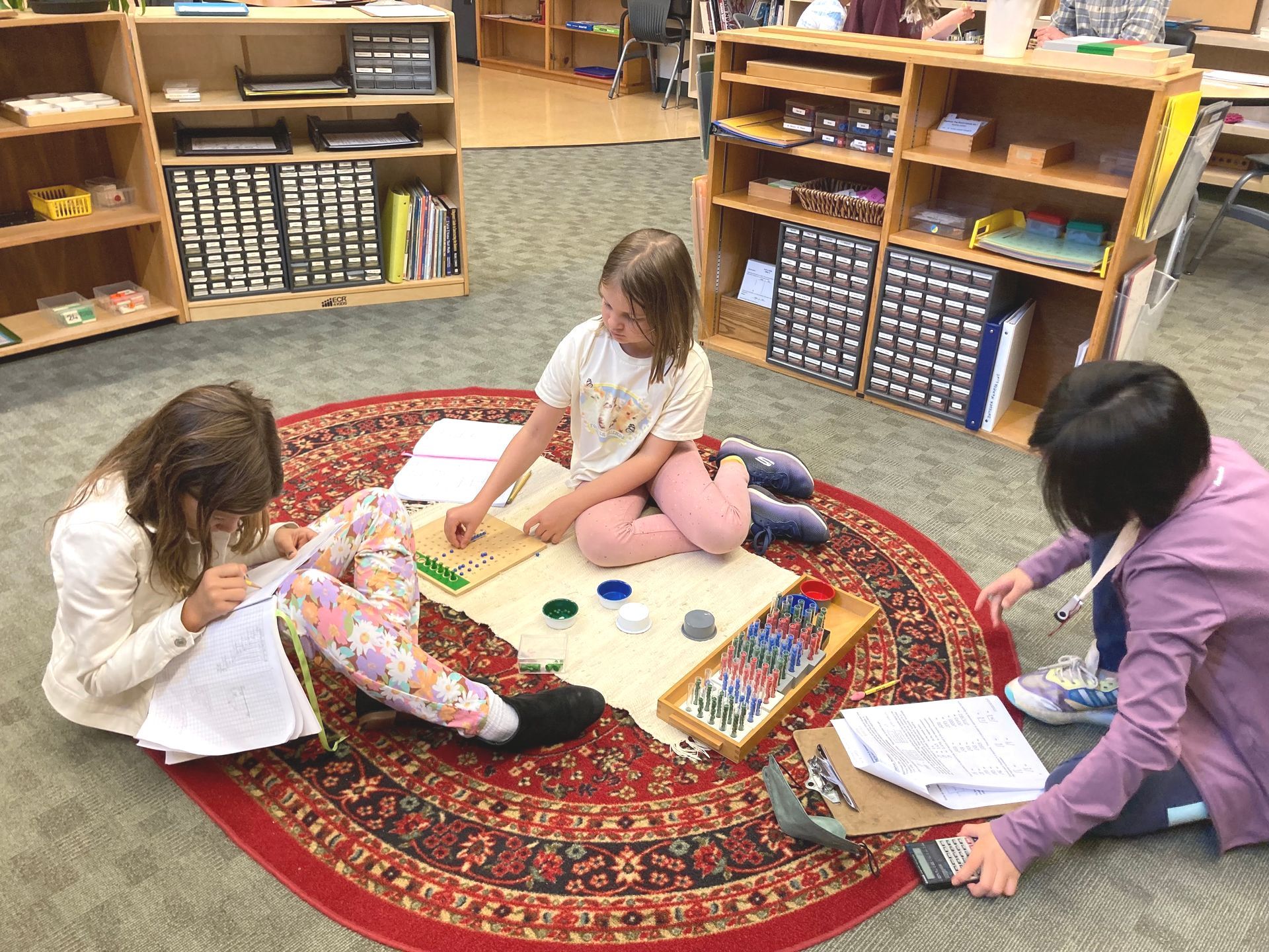 Three Upper Elementary students working together with Montessori division materials in the Montessori Elementary classroom.