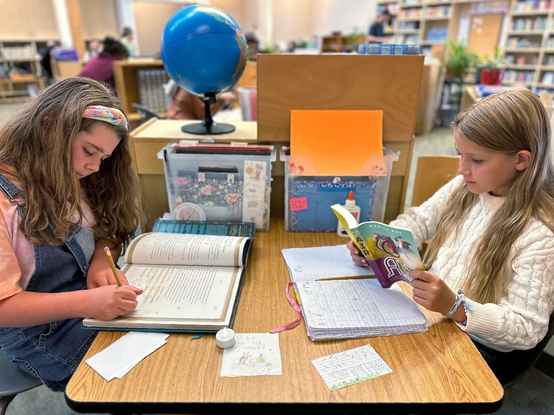 Two Upper Elementary students sitting together reading a book quietly.