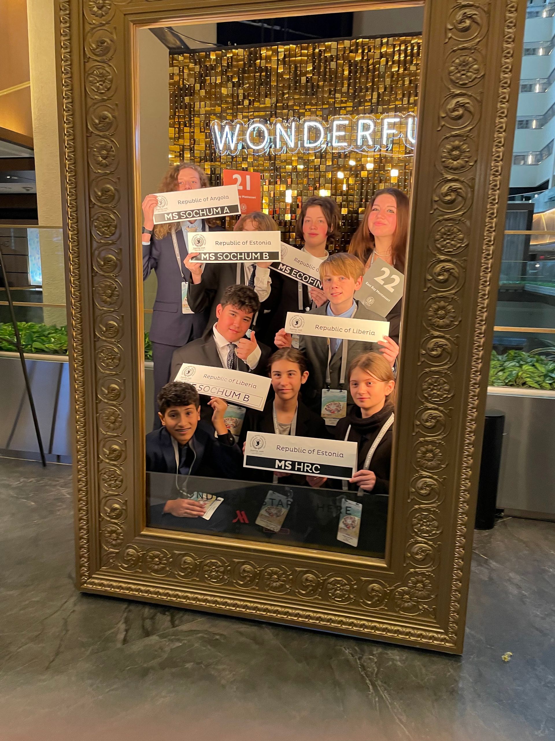 The Middle School group smile in a giant gold frame while holding up their MMUN labels.