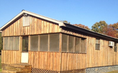 Weathered wooden cabin with screened porch and small windows under a clear blue sky