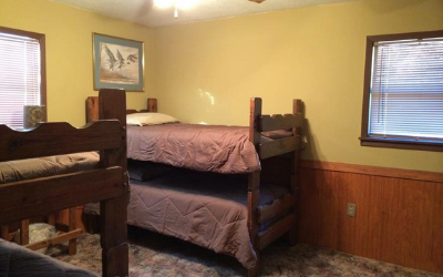 Bedroom with two wooden bunk beds, tan walls, and windows letting in daylight.
