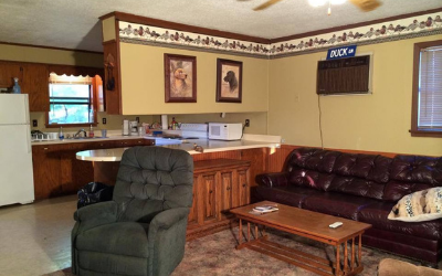 Cozy living room with brown couch, green recliner, coffee table, and kitchen visible in the background