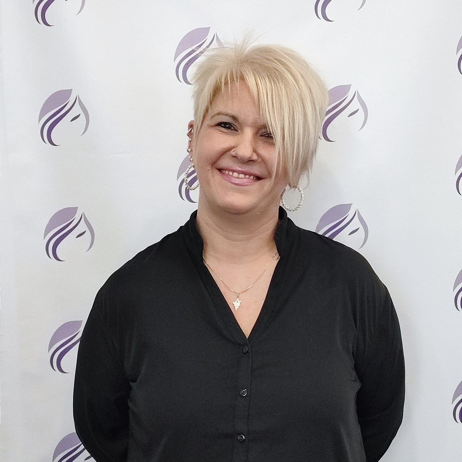Eine Frau in einem schwarzen Hemd lächelt vor einem violetten Hintergrund