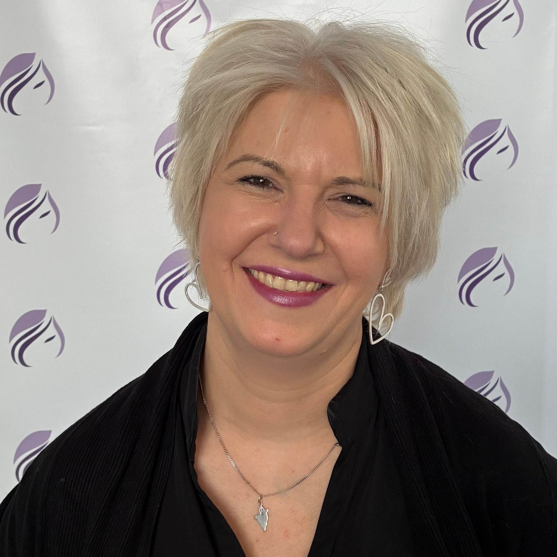 Eine Frau in einem schwarzen Hemd lächelt vor einem violetten Hintergrund