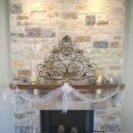 Decorative wrought-iron wall art and white ribbon garland above a fireplace mantel on a stone wall