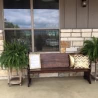 Front porch with a wooden bench, two potted plants, and a house window behind it.