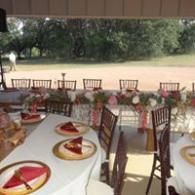 Outdoor banquet setup with white tablecloths, red napkins, and chairs overlooking a lawn and trees