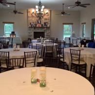 Elegant banquet hall with round tables, white tablecloths, black chairs, and a chandelier centered by a fireplace