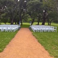 Outdoor wedding aisle with white chairs on both sides of a dirt path under trees