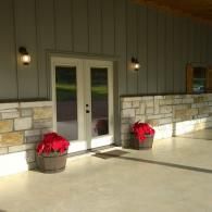 Double doors on a building entrance with two red potted flowers on a sunny porch