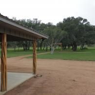 Covered patio overlooking a sandy field and grassy park with scattered trees under an overcast sky